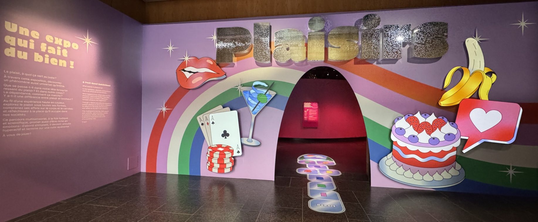 Entrée de l'exposition Plaisirs : arche arc-en-ciel et décor de lèvres, cocktail, gâteau et banane